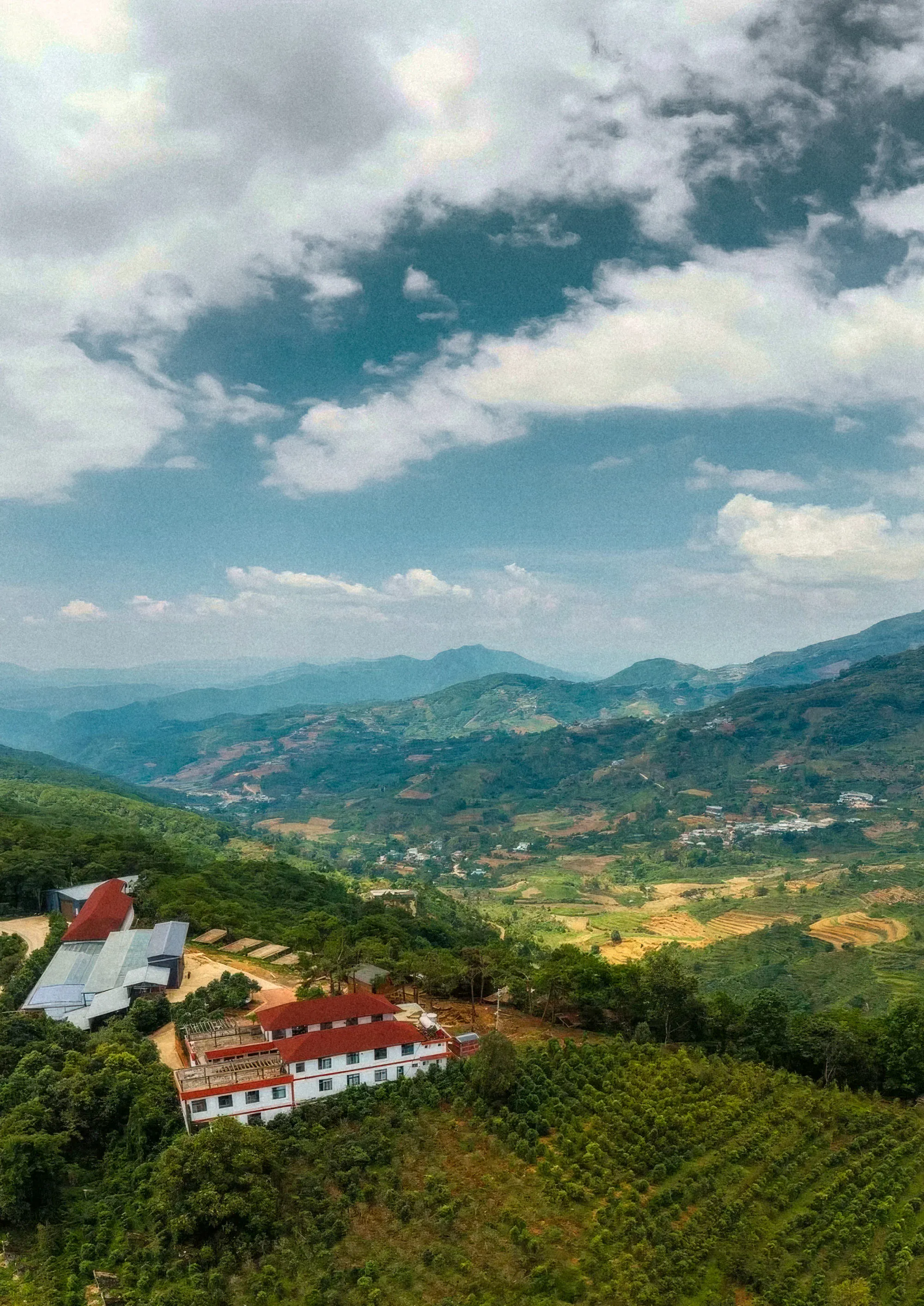 Aerial view of a Yunnan valley: the farm and its sheds in the foreground, coffee plots and mountains beyond